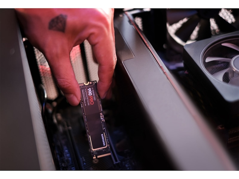 A hand installing the Samsung 990 PRO 2TB NVMe SSD into an M.2 slot inside a PC case, next to a graphics card cooler.