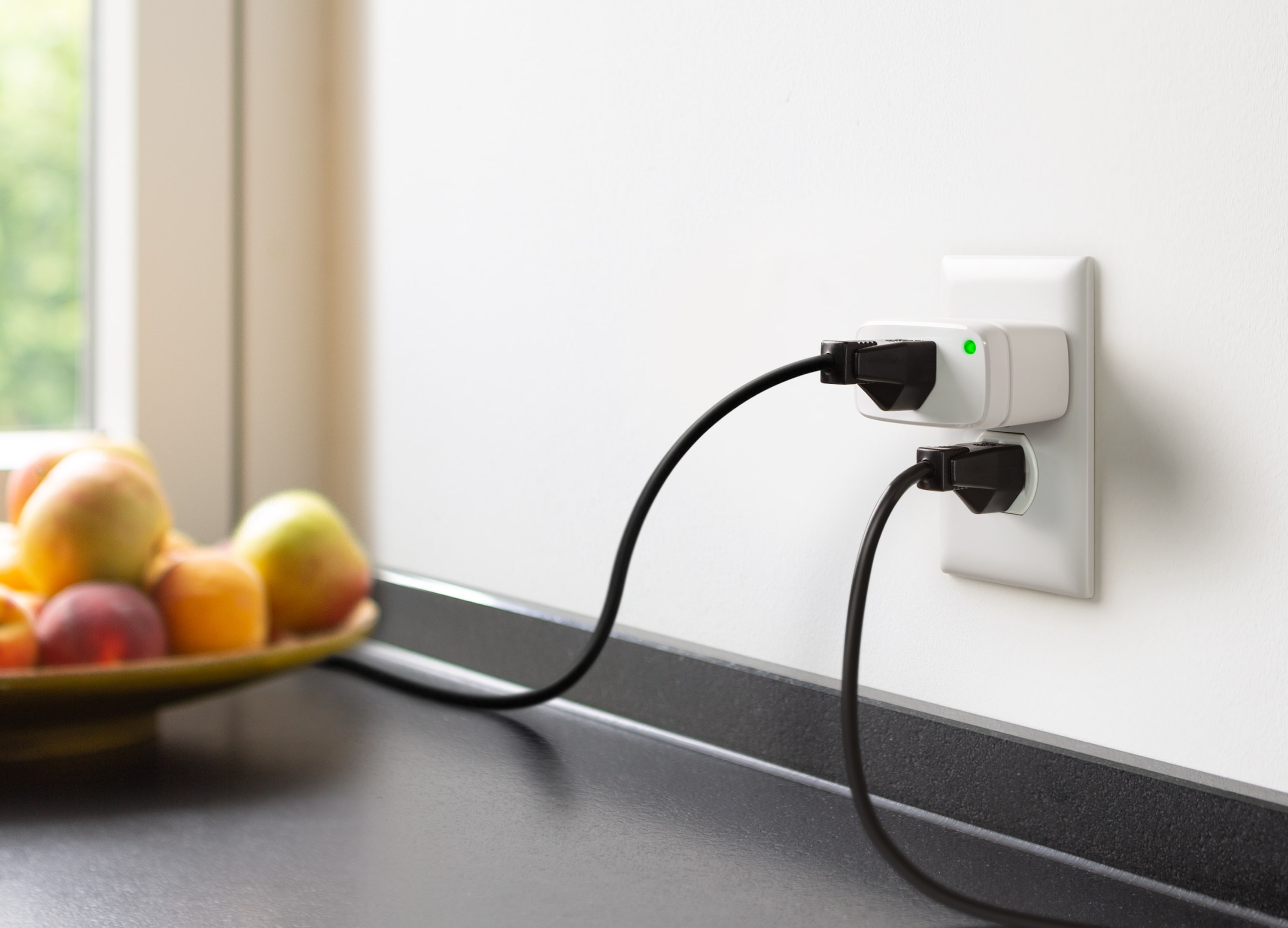 Eve Energy smart plug installed in a US wall outlet in a kitchen, with a lamp cord plugged into it