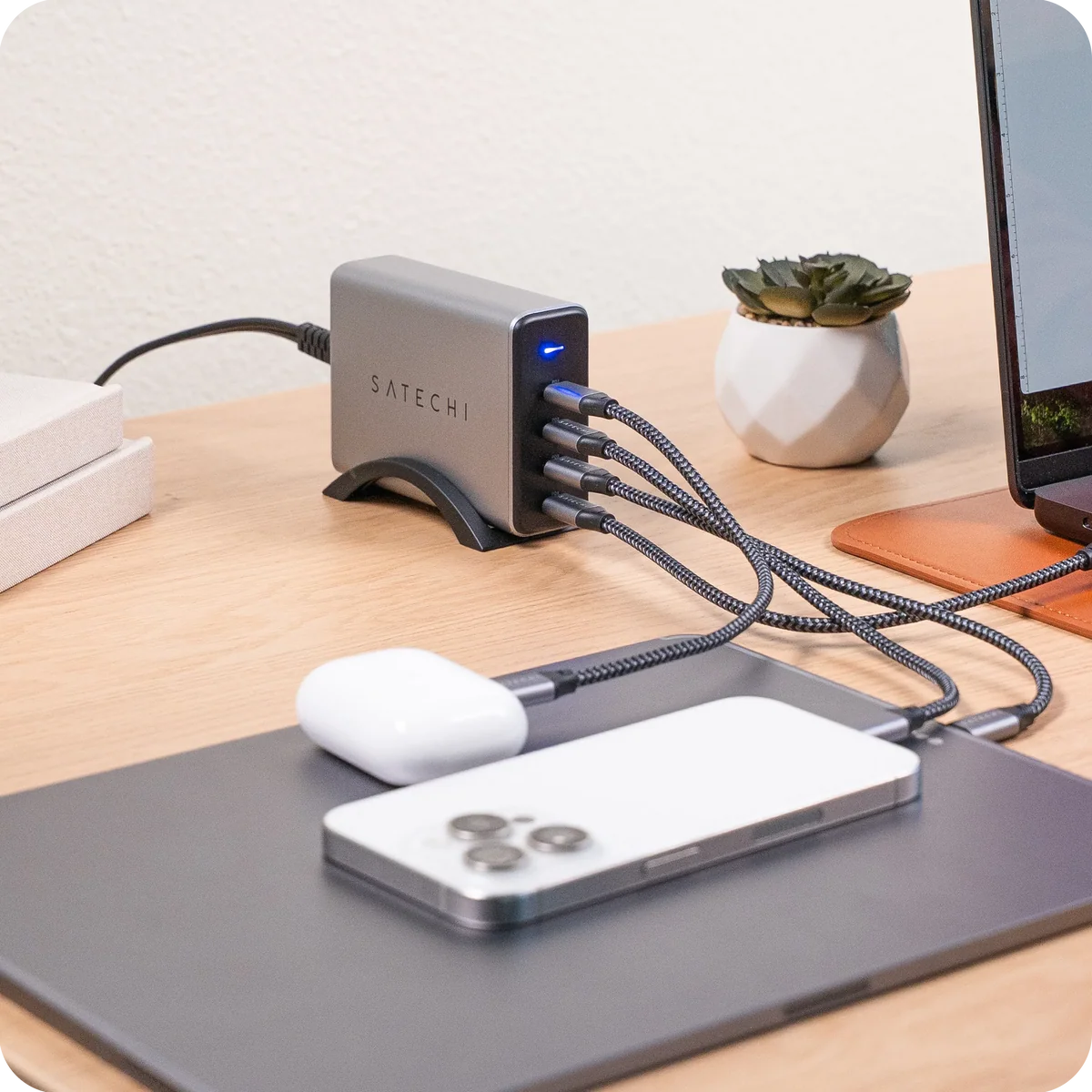 Satechi 165W USB-C 4-Port PD GaN Charger in use on a desk, charging a phone, earbuds and a laptop