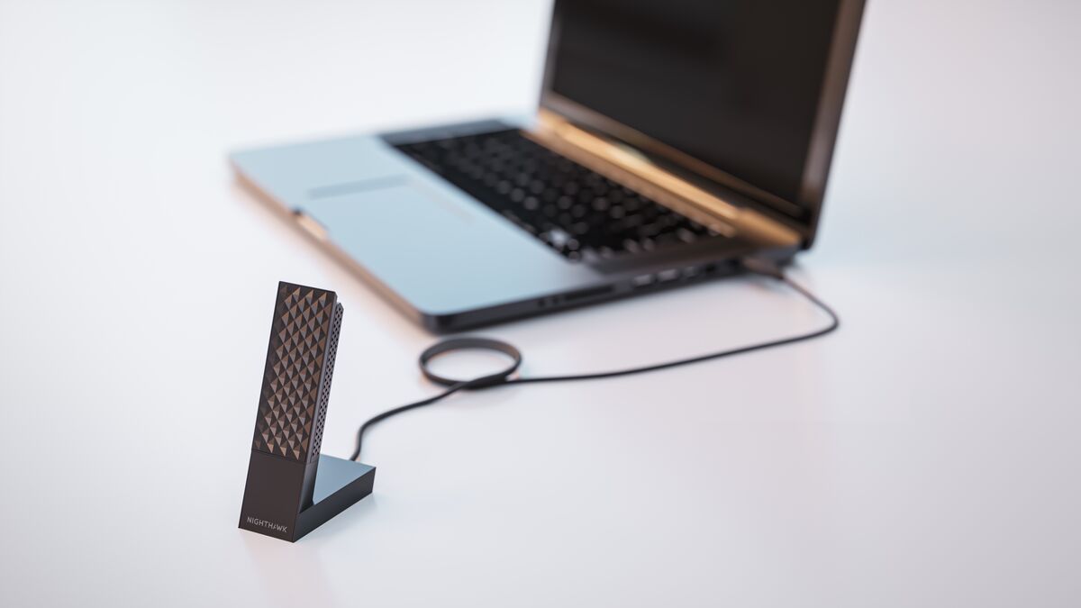 Black NETGEAR Nighthawk A9000 standing in its cradle beside a laptop connected by USB cable
